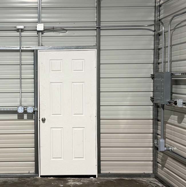 White door in a metal-paneled wall with exposed electrical conduits by a licensed electrician.