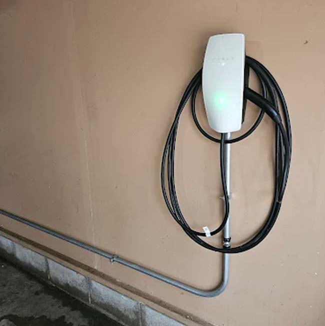 Wall-mounted electrical vehicle charger with coiled black cable, installed by a licensed & insured pro.