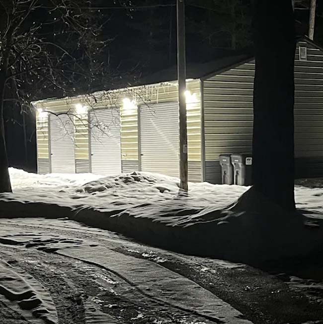 A metal garage with bright lights and snow in Wisconsin Rapids at night, licensed & insured.