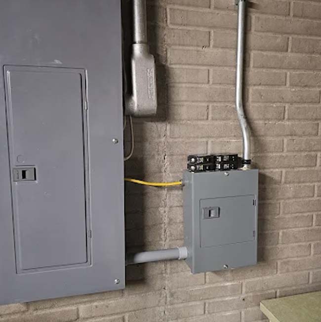 Two gray electrical panels on a brick wall, wired by a licensed & insured electrician.