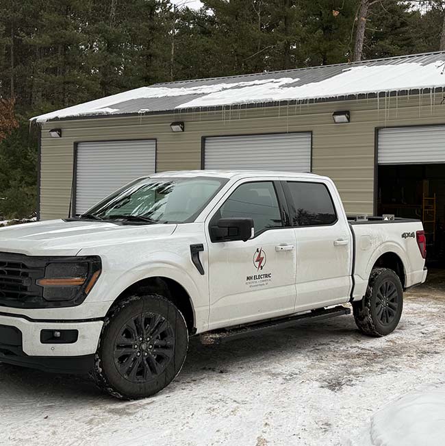 White pickup with JW Electric logo parked by a garage in snowy Wisconsin Rapids. Electrical work.