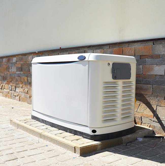 A white standby generator sits on a paved area in Wisconsin Rapids by a stone wall.