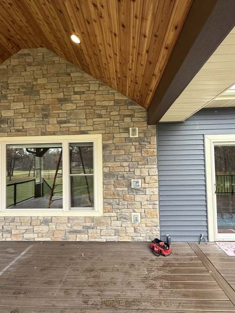 Covered porch in Wisconsin Rapids with stone wall, wood ceiling, and items on the wooden floor.